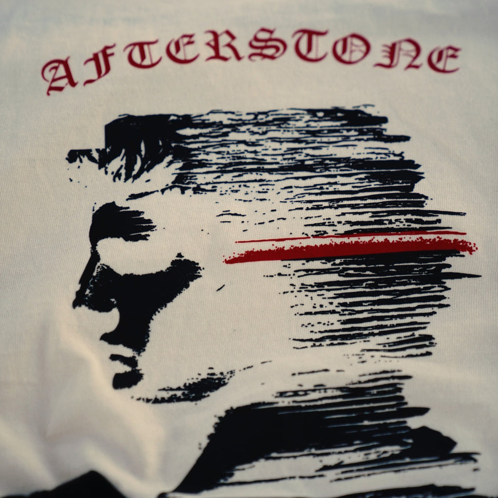 STRATUM HEAD print close-up on ivory cotton — red AFTERSTONE wordmark above the graphic