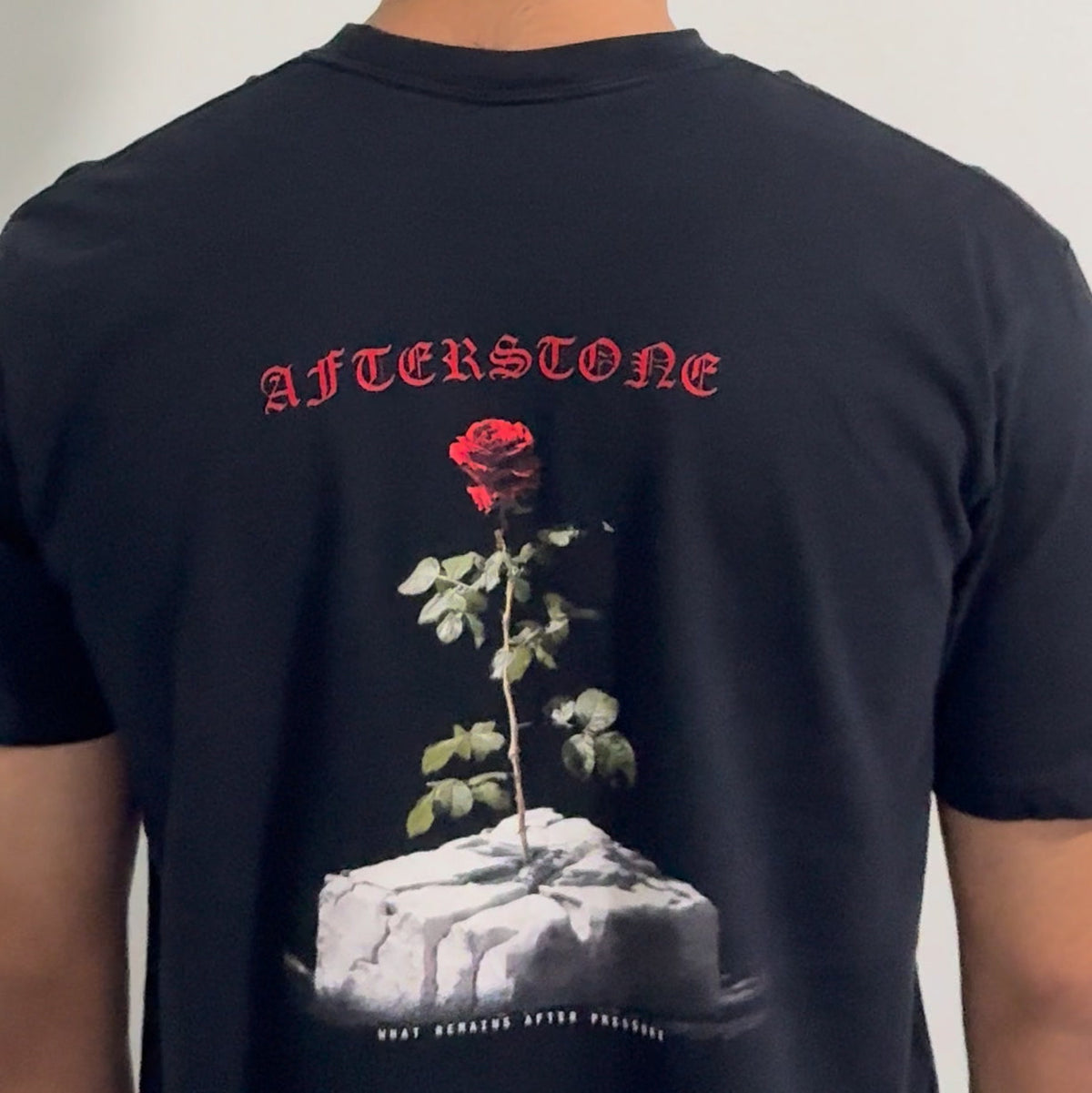 The black GREW ANYWAY heavyweight tee worn — a rose growing out of cracked stone printed large across the back