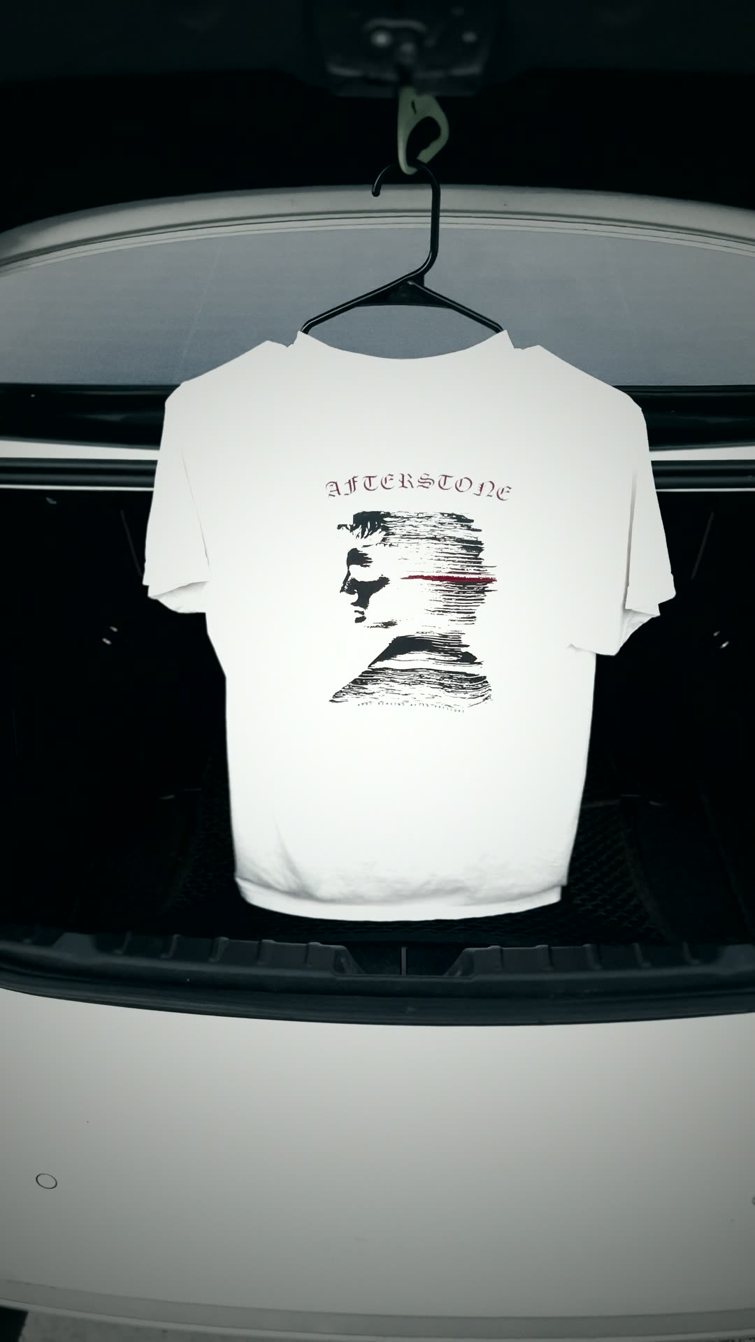 The ivory Stratum Head tee hanging in an open car trunk at golden hour
